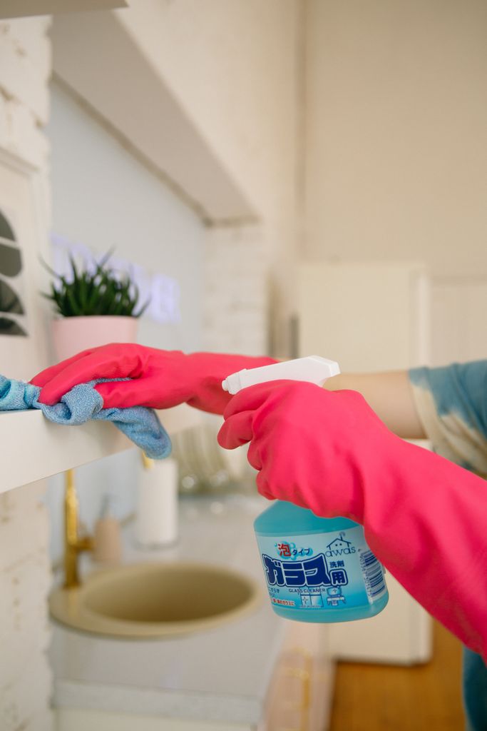 Photo by Polina Zimmerman Person using spray bottle and cloth for cleaning a kitchen shelf, ensuring hygiene and cleanliness.